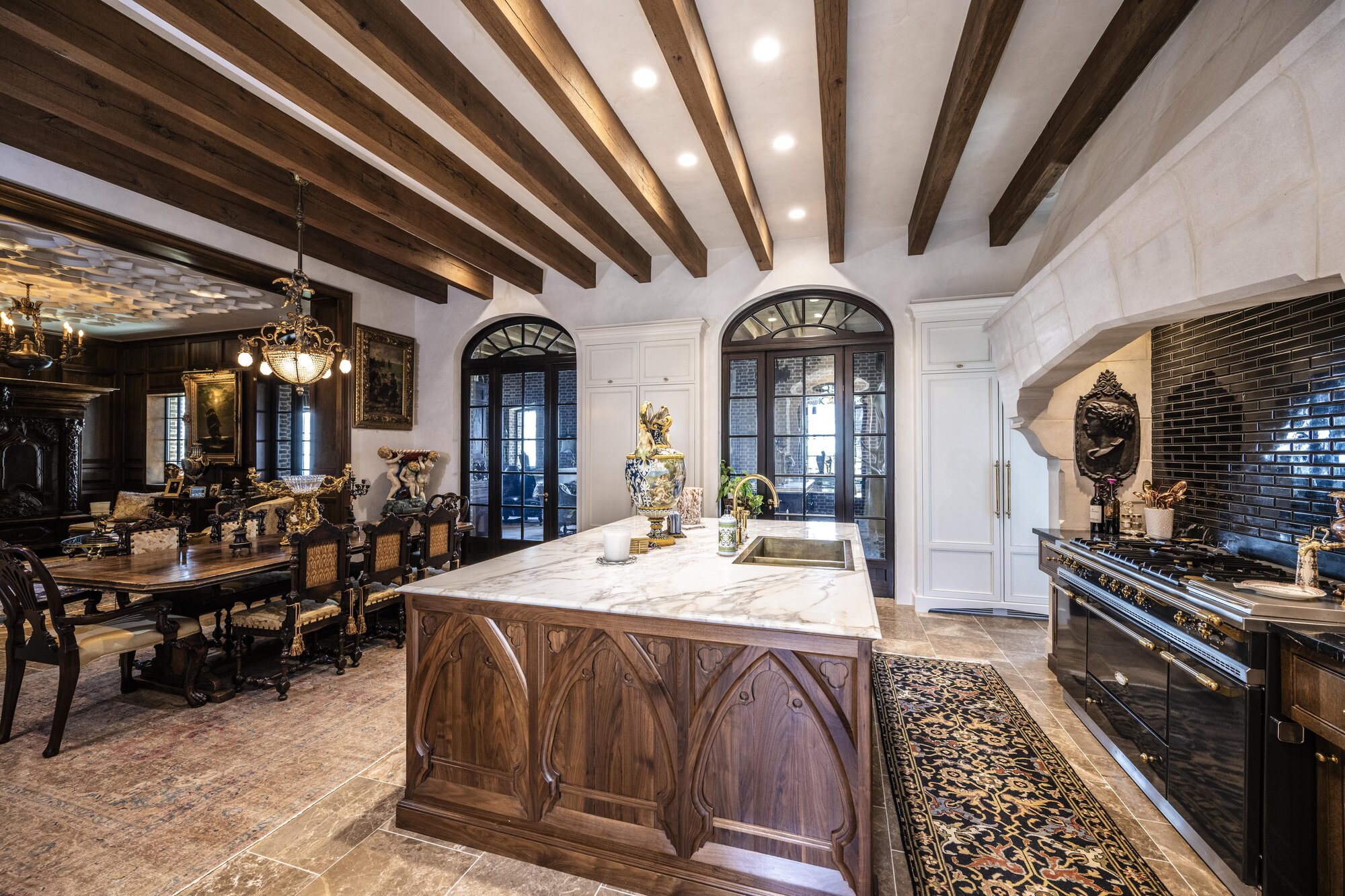 Editorial view of a residential kitchen with cream Venetian plaster walls beneath dark wood beams, Ravencliff Residence